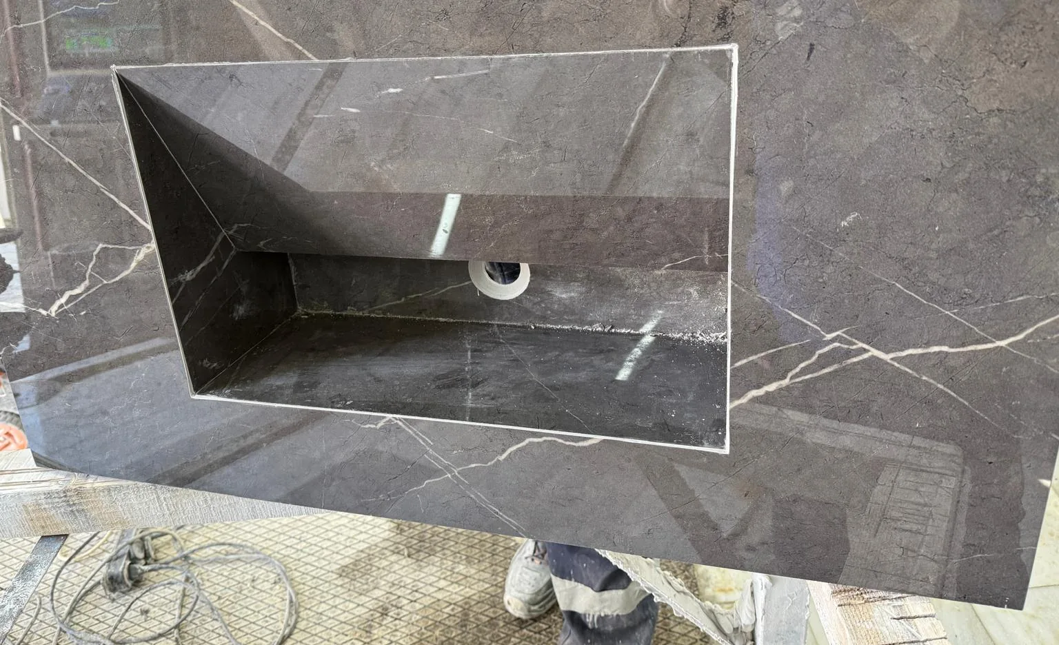 Antrasit mermer banyo tezgahı — tezgahın kendi taşından oyulmuş dikdörtgen lavabo teknesi ve gider deliği, atölyede montaj öncesi